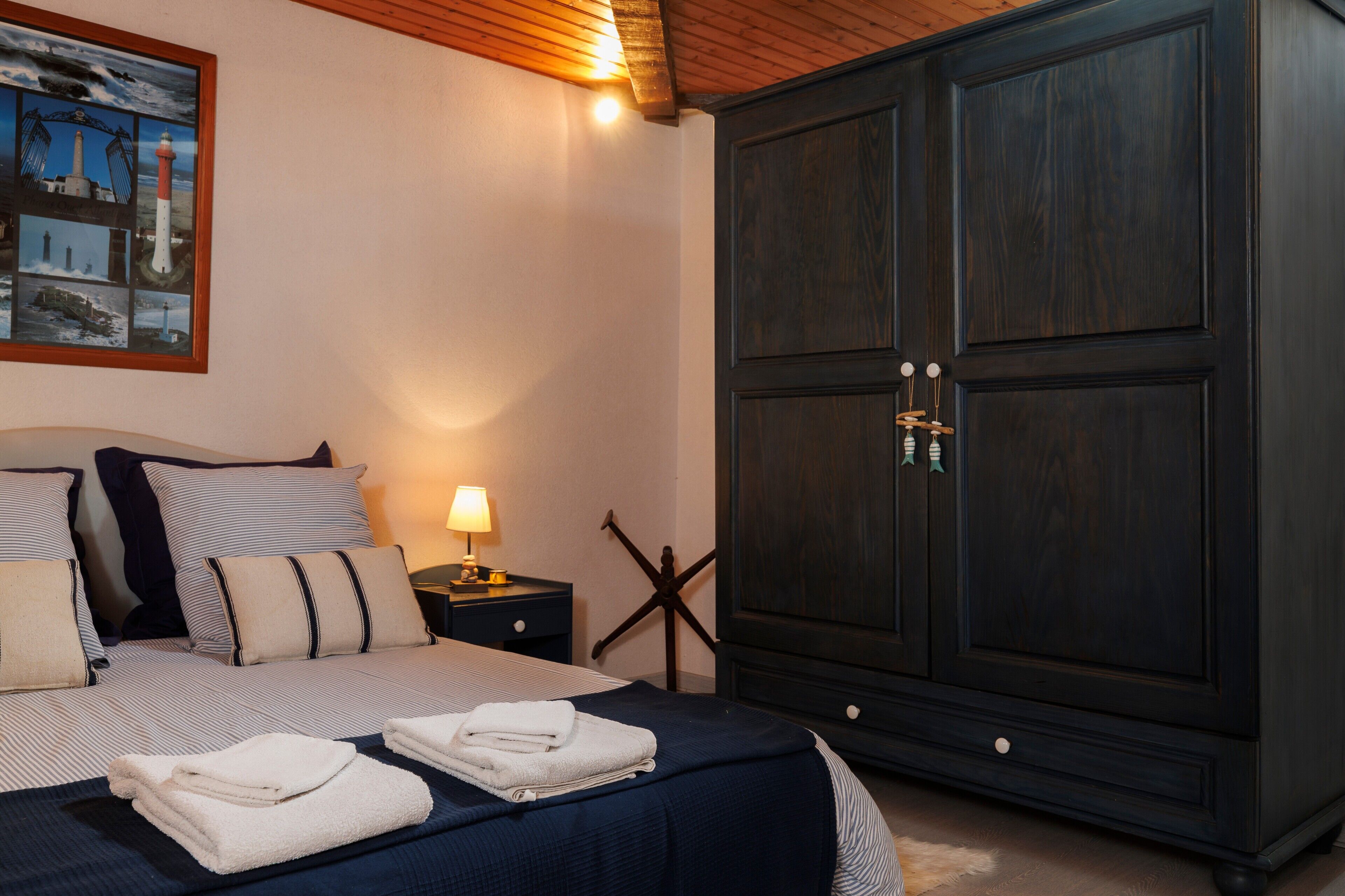 A bedroom with a bed, pillows, a nightstand with a lamp, a large wardrobe, and a wall-mounted picture.