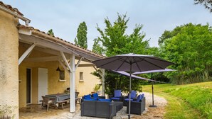 Une terrasse extérieure avec un sol en pierre, des meubles en osier et un grand parasol.