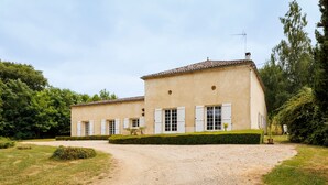 Un bâtiment à deux étages avec une allée gravillonnée, des volets blancs et un petit jardin.