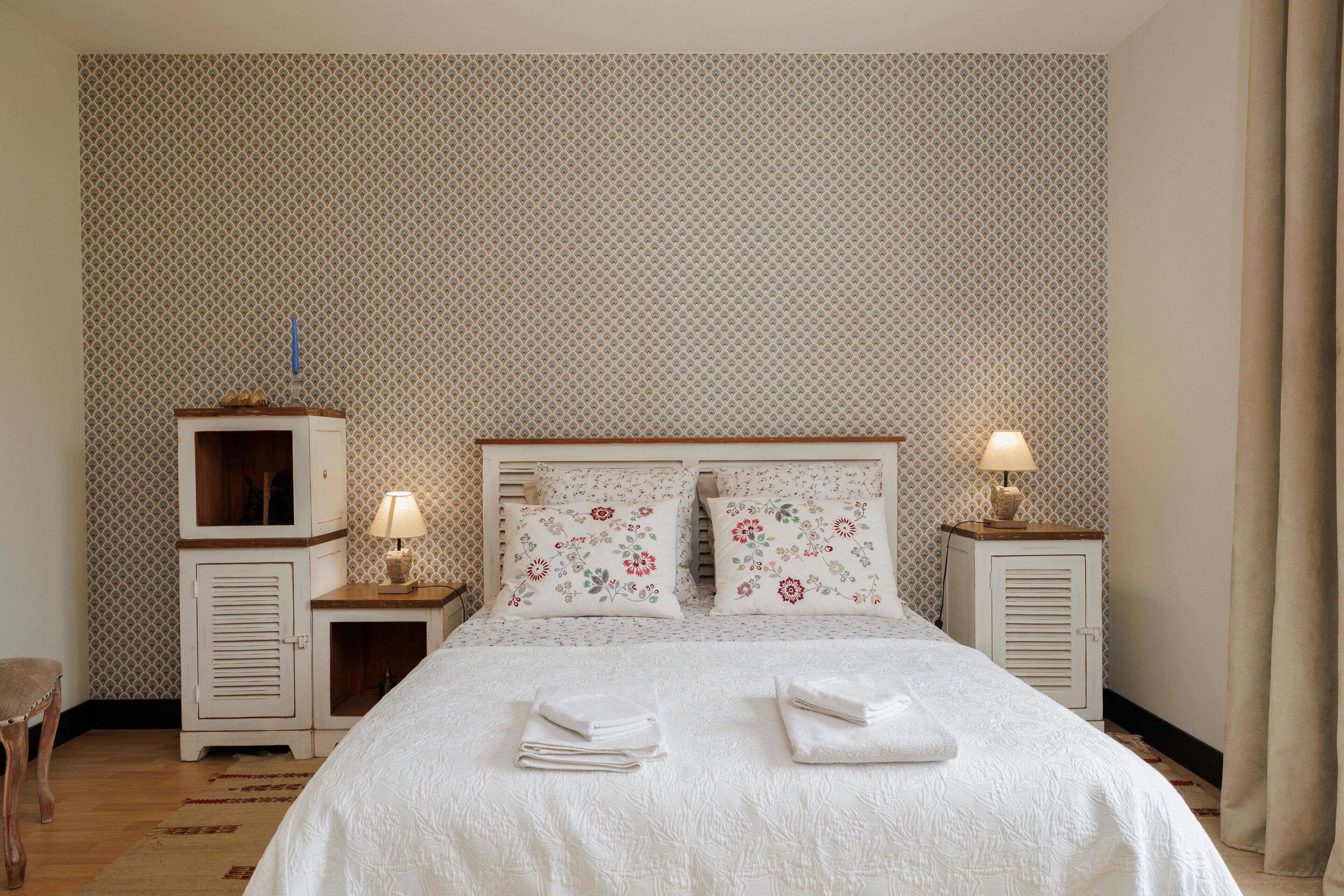 A neatly arranged hotel room with a large bed, two bedside tables with lamps, a wardrobe, and a patterned wall.