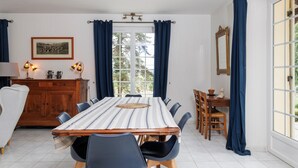 Un coin repas comprenant une table, des chaises, un buffet en bois et une fenêtre avec des rideaux.