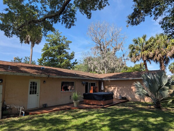 A single-story house with a covered patio, a lawn, and surrounding trees.