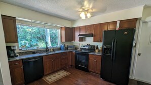 Una cocina con armarios de madera, un refrigerador negro, una estufa y una ventana con vistas a la vegetación.