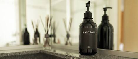 A hand soap bottle on a countertop with a mirror reflecting various bathroom items.