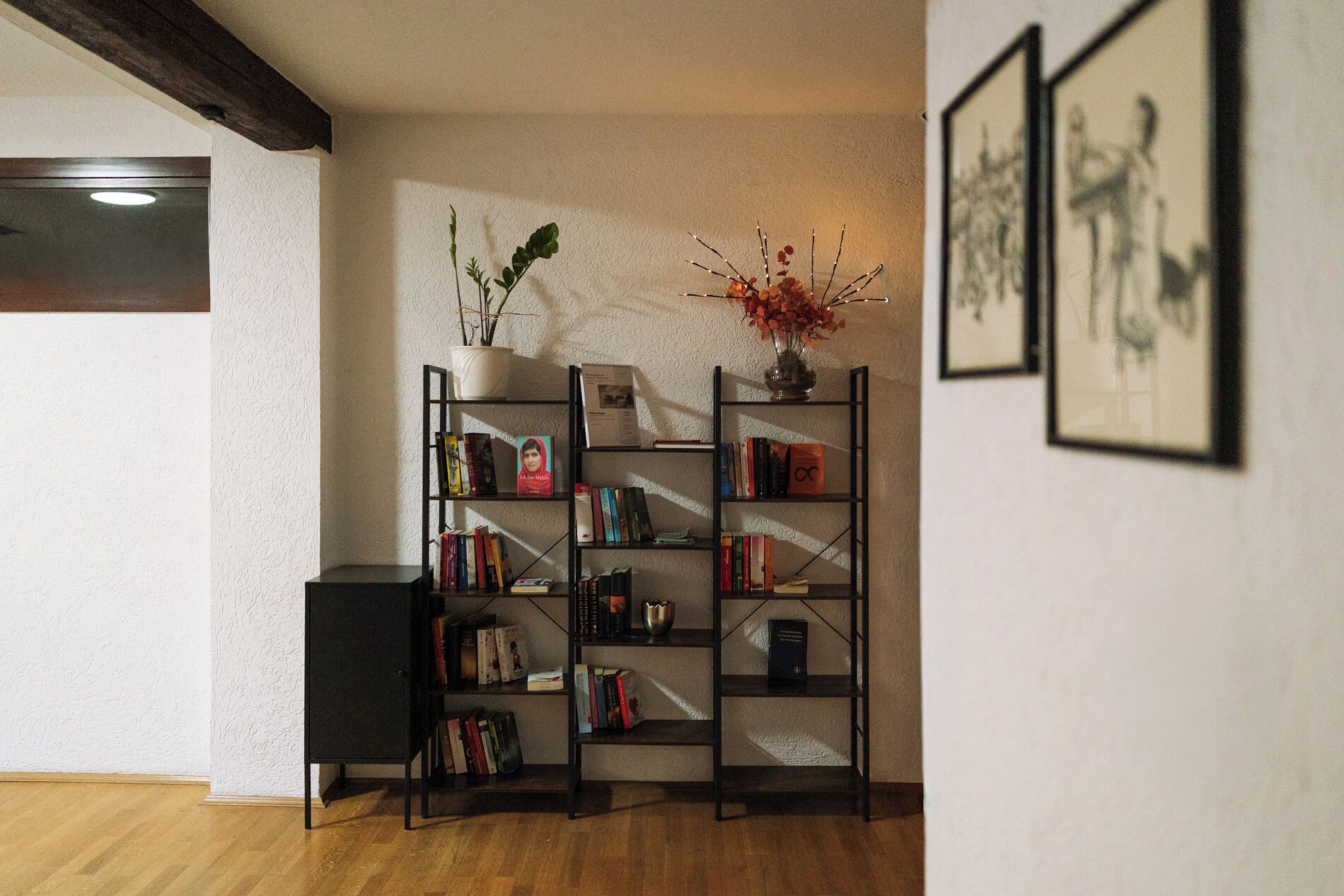 A room with wooden flooring, a bookshelf, a small table, and framed artwork on the wall.
