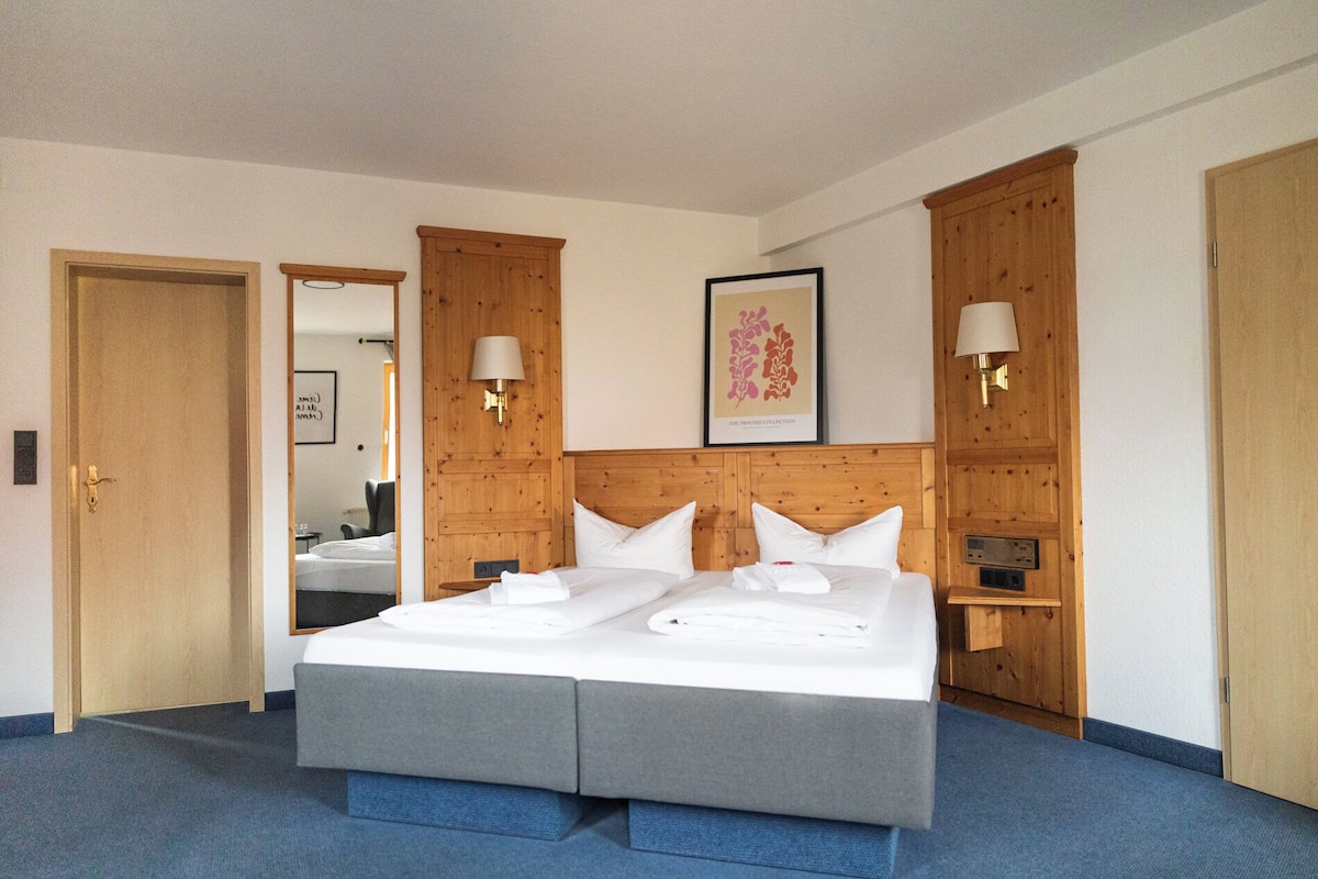 Une chambre d’hôtel avec un grand lit, une tête de lit en bois, deux tables de chevet, une lampe fixée au mur et un tableau encadré.