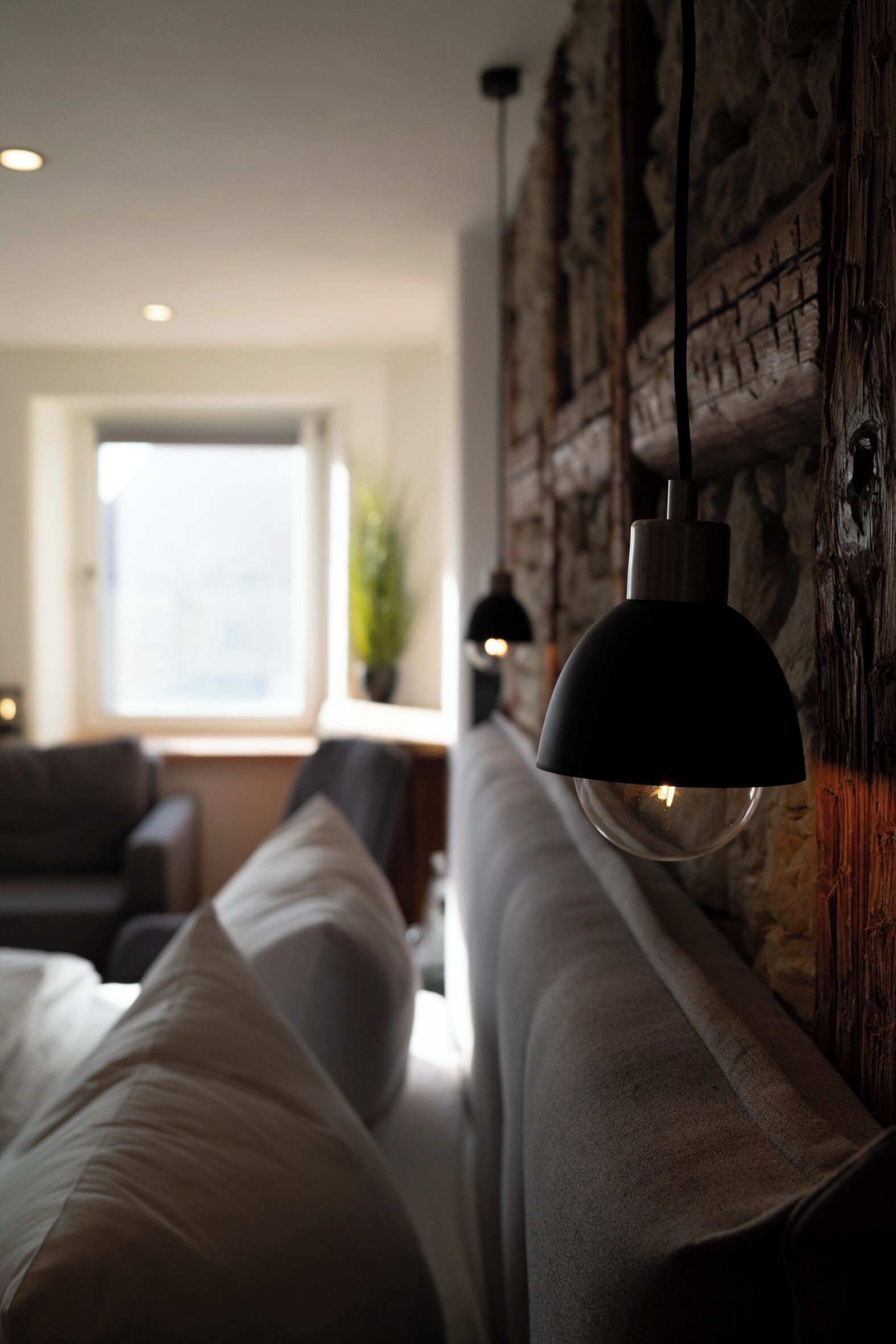 A modern bedroom with a large bed, a hanging pendant light, and a stone wall.