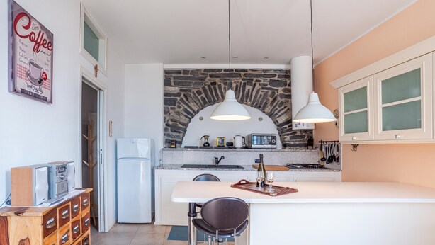 A modern kitchen with a stone arch, white cabinets, and a bar area with stools. - Casa Valleggia (Moltrasio)