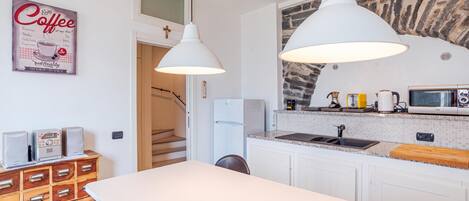 A modern kitchen with white cabinets, a granite countertop, and a stone backsplash. There are two pendant lights, a coffee-themed poster, and a microwave on the counter.
