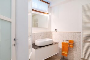 A bathroom with a white sink, a mirror, and a towel rack with an orange towel.