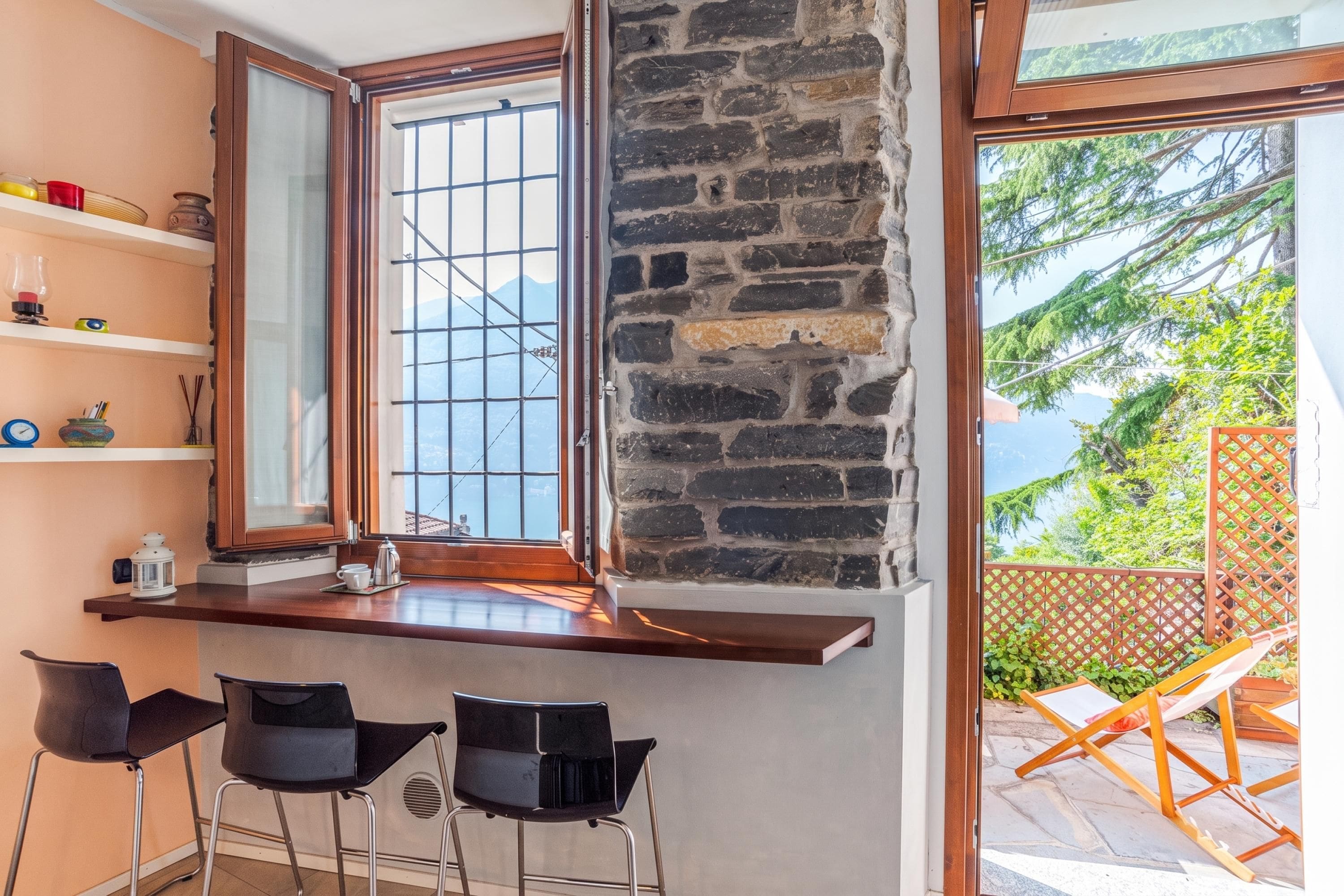 A room with a stone wall, a window with a view of greenery, and a bar area with chairs.