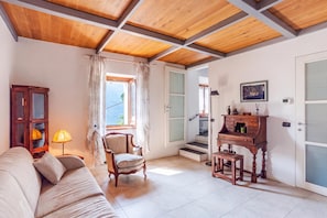 Quarto com teto de madeira, sofá, poltrona, escrivaninha com gavetas e janela com cortinas.