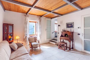 Una habitación con techo de madera, un sofá, una silla, un escritorio con cajones y una ventana con cortinas.
