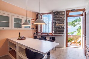 A modern kitchen with a white countertop, two pendant lights, and a view of the outdoors through a glass door.