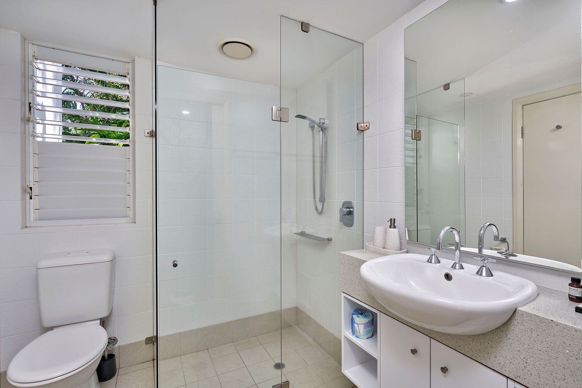 Un baño moderno con cabina de ducha de vidrio, un lavabo blanco y un inodoro.