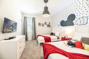 Habitación de hotel con dos camas, televisión, escritorio y pared con un mural de Mickey Mouse.