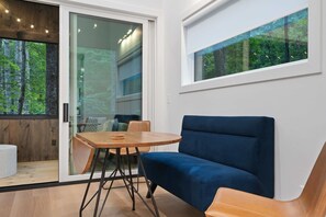 A modern living room with a blue sofa, a wooden coffee table, and a glass door leading to a balcony with a forest view. - Modern 2BR Cabin near Highlands · Secluded Wooded Setting (Highlands)