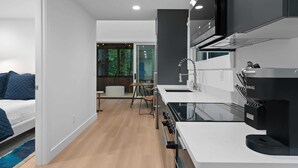 Una cocina moderna con una cafetera negra, una encimera blanca y vistas al exterior a través de una puerta de vidrio.