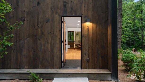 Fachada de madera con una puerta que da a un interior con un comedor visible.