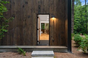 A wooden exterior with a door leading to an interior with a visible dining area. - Modern 2BR Cabin near Highlands · Secluded Wooded Setting (Highlands)