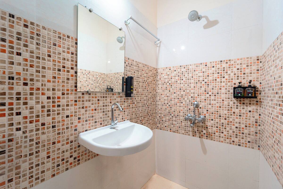 A bathroom with a mosaic tile wall, a white sink, a handheld showerhead, and a handheld shower bar.