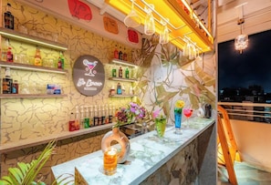 A bar area with shelves of bottles, a neon sign, and decorative plants.
