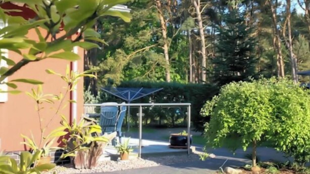 A residential area with a paved driveway, a small garden with various plants, a metal structure, and a building in the background. - Vacation home Maria by Interhome (Zinnowitz)