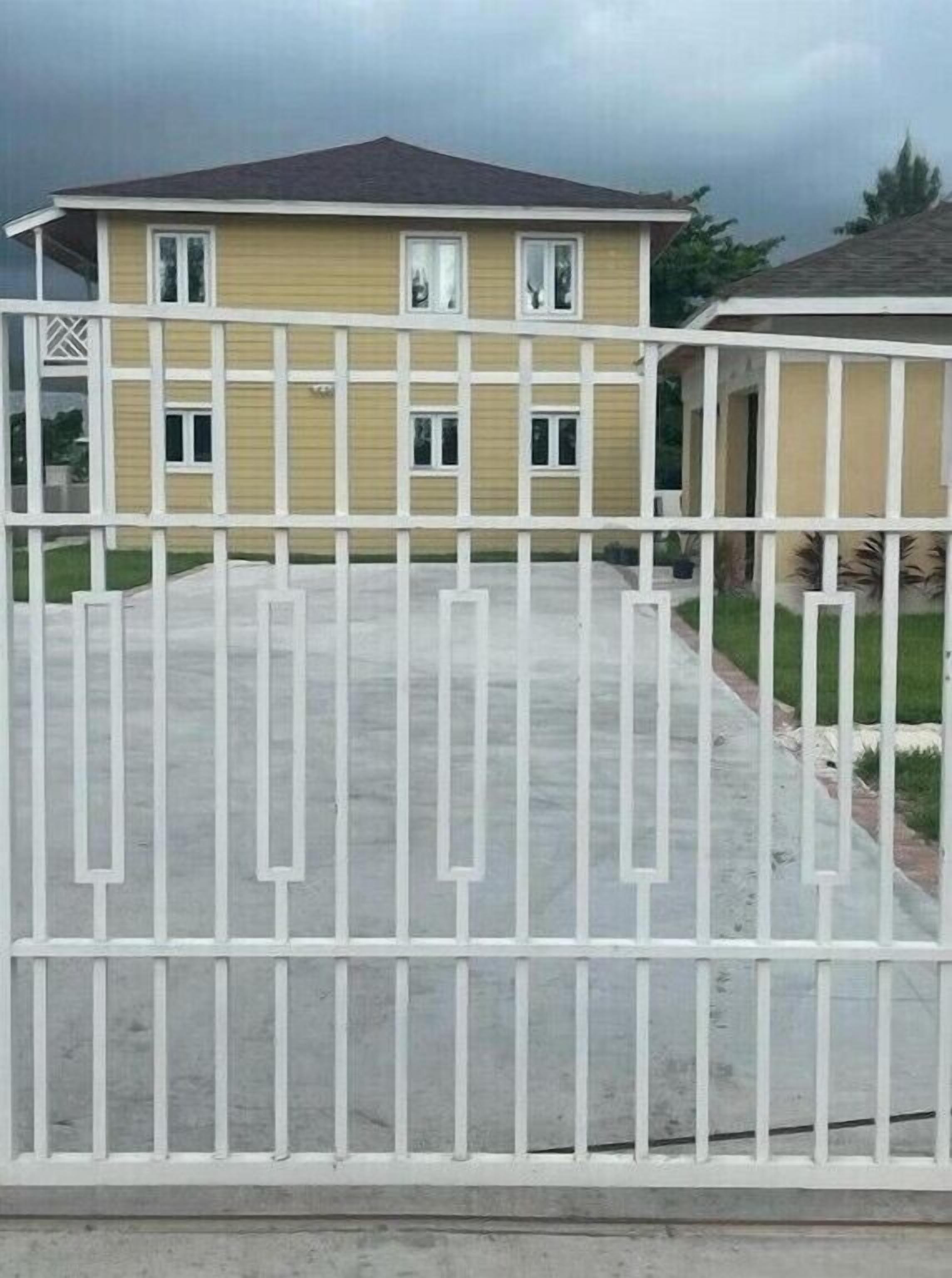 A residential house with a fenced driveway, a garage, and a well-maintained lawn.