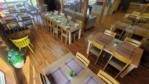 Un restaurante con varias mesas y sillas de madera, una zona de bar y una pantalla de televisión.