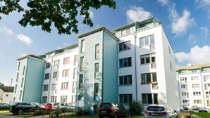 Ein mehrgeschossiges Wohngebäude mit modernem Design, das weiße und türkise Farbtöne kombiniert.