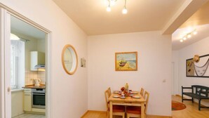 Ein Essbereich mit einem Holztisch und -stühlen, einem Bild an der Wand und einer durchgehenden Tür erkennbaren Küche.