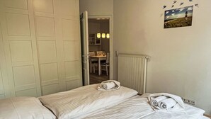 A hotel room with two beds, a radiator, a dining area, and a wall with a picture of birds flying.