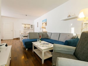 Ein modernes Wohnzimmer mit einem Ecksofa, einem Couchtisch und einem Essbereich im Hintergrund.