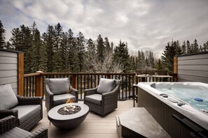 A deck with wicker furniture, a fire pit, and a hot tub. - Luxury Townhome | Private Hot Tub & Fire Table (Canmore)