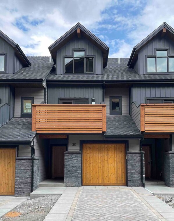 A modern multi-story residential building with a symmetrical facade, large windows, and a prominent balcony. - Luxury Townhome | Private Hot Tub & Fire Table (Canmore)
