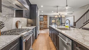 Una cucina moderna con mobili scuri, un piano di lavoro in marmo, elettrodomestici in acciaio inossidabile e un pavimento in legno.