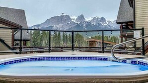 A hot tub with a mountain view, surrounded by a deck with a railing. - Wake Up to Three Sisters | Penthouse Condo (Canmore)