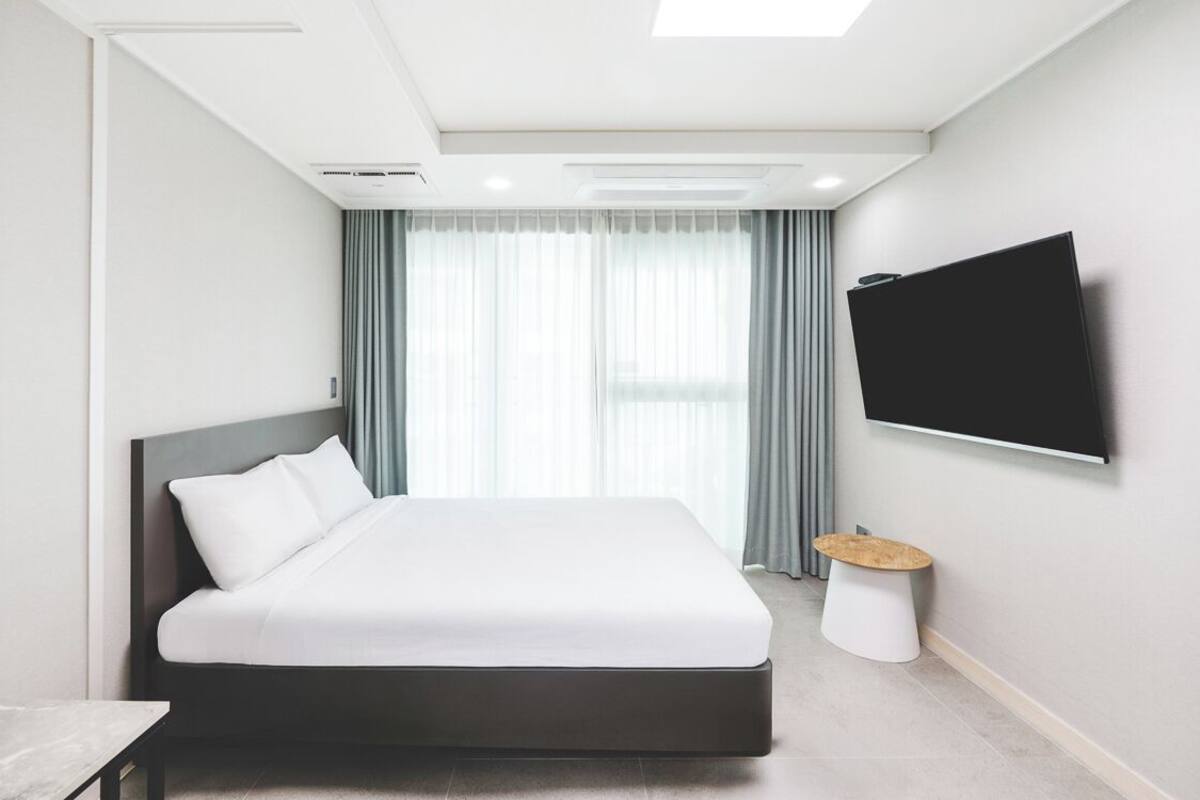 Une chambre d’hôtel moderne avec un grand lit, un téléviseur à écran plat fixé au mur et une petite table ronde.