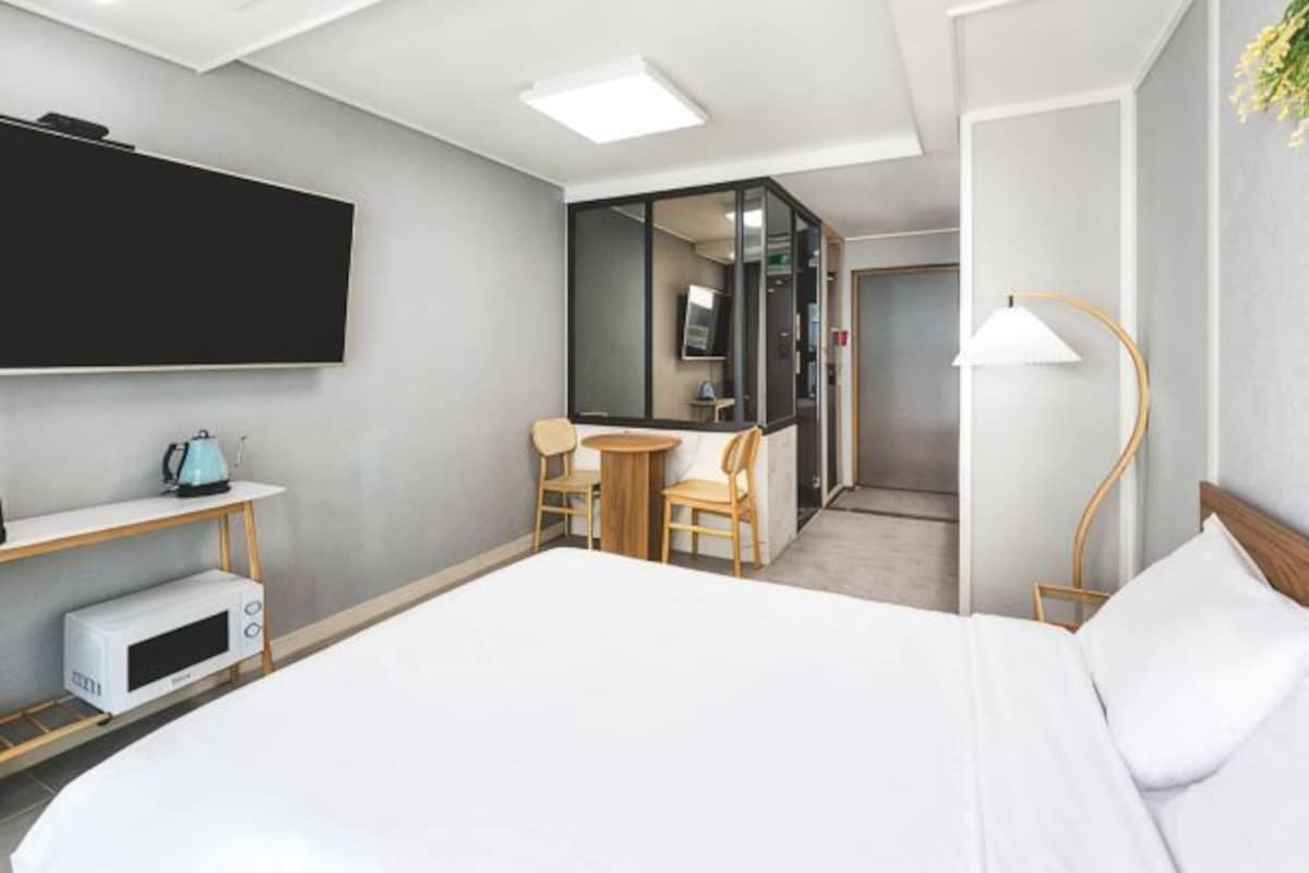 A hotel room with a bed, a TV, a microwave, a desk with chairs, and a lamp.