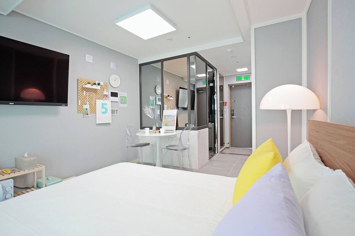 Une chambre d’hôtel équipée d’un lit, d’un bureau, d’une chaise, d’une télévision, d’une lampe et d’une cloison en verre.