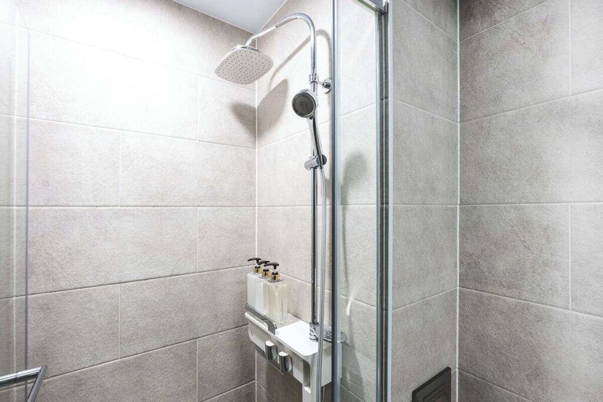 Une douche moderne dotée d’un pommeau de douche à main, d’un panneau de commande mural et d’un espace de douche délimité par des parois en verre.
