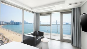 A modern hotel room with a large balcony, a bed, a sofa, and a TV.