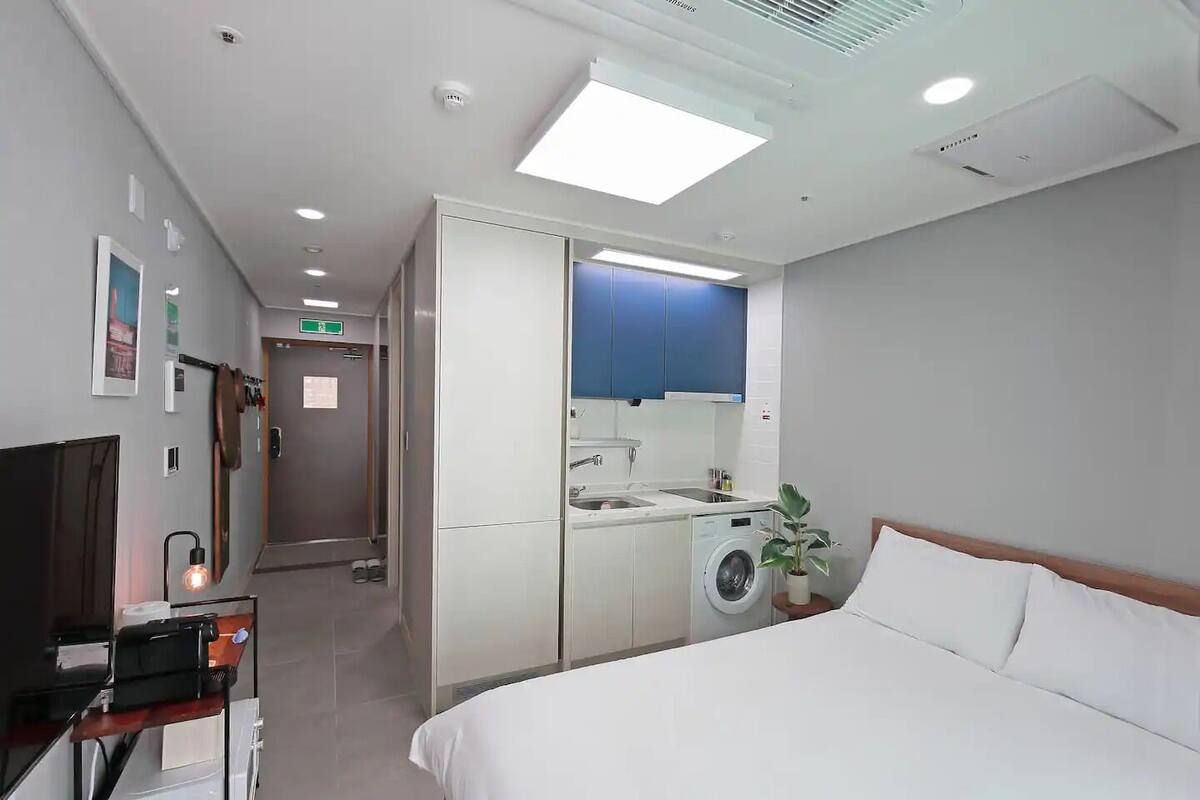 Une chambre d’hôtel équipée d’un lit, d’une machine à laver, d’un lavabo et d’un petit coin cuisine.