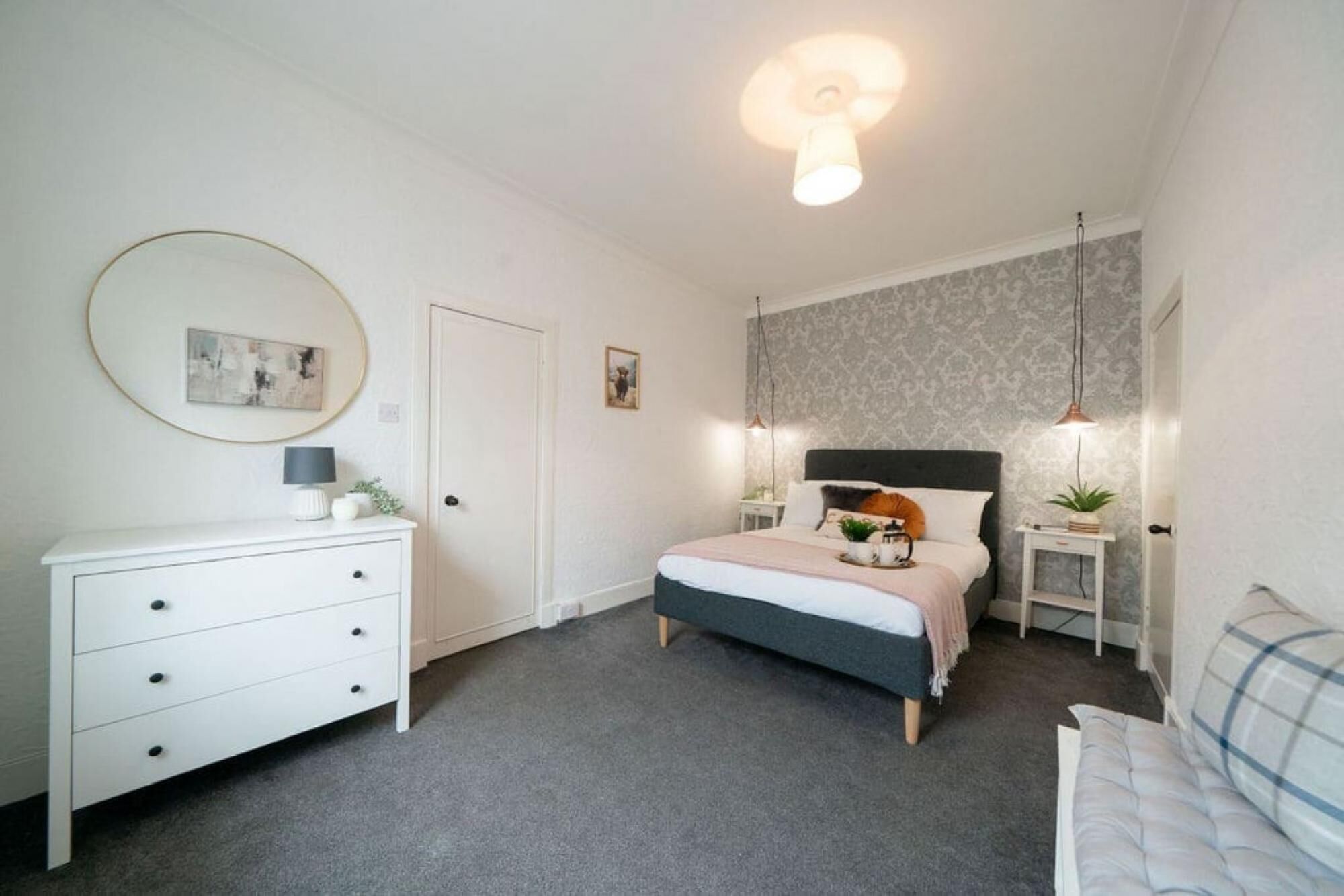 Quarto com cama, cómoda, mesa de cabeceira, luminária e iluminação no teto.