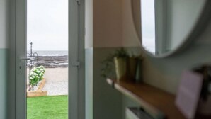 Vista a través de una puerta que da a una playa con una terraza de madera y una zona verde.