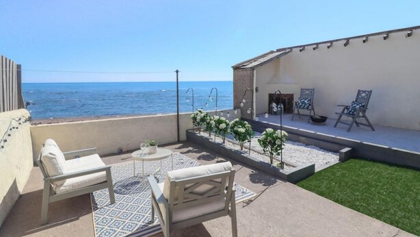 Una terraza con vistas al mar, mobiliario exterior y un pequeño jardín.