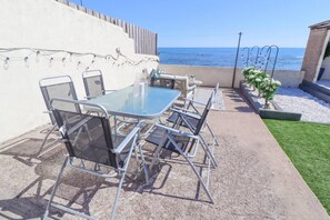 Une terrasse extérieure avec une table en verre et des chaises en métal, donnant sur la mer.