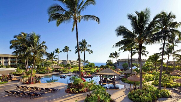 Een resort met een groot zwembad, palmbomen en uitzicht op de oceaan.