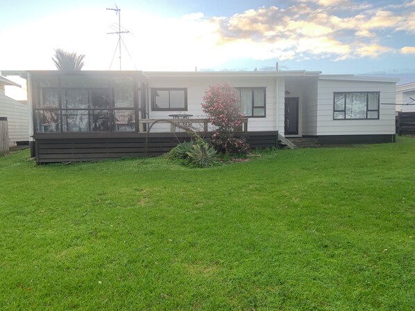 A single-story mobile home with a covered porch, a small garden with pink flowering plants, and a clear sky. - Waterfront - 3 bedroom, 2 bathroom, peaceful, private with- sunny conservatory (Glenbrook)