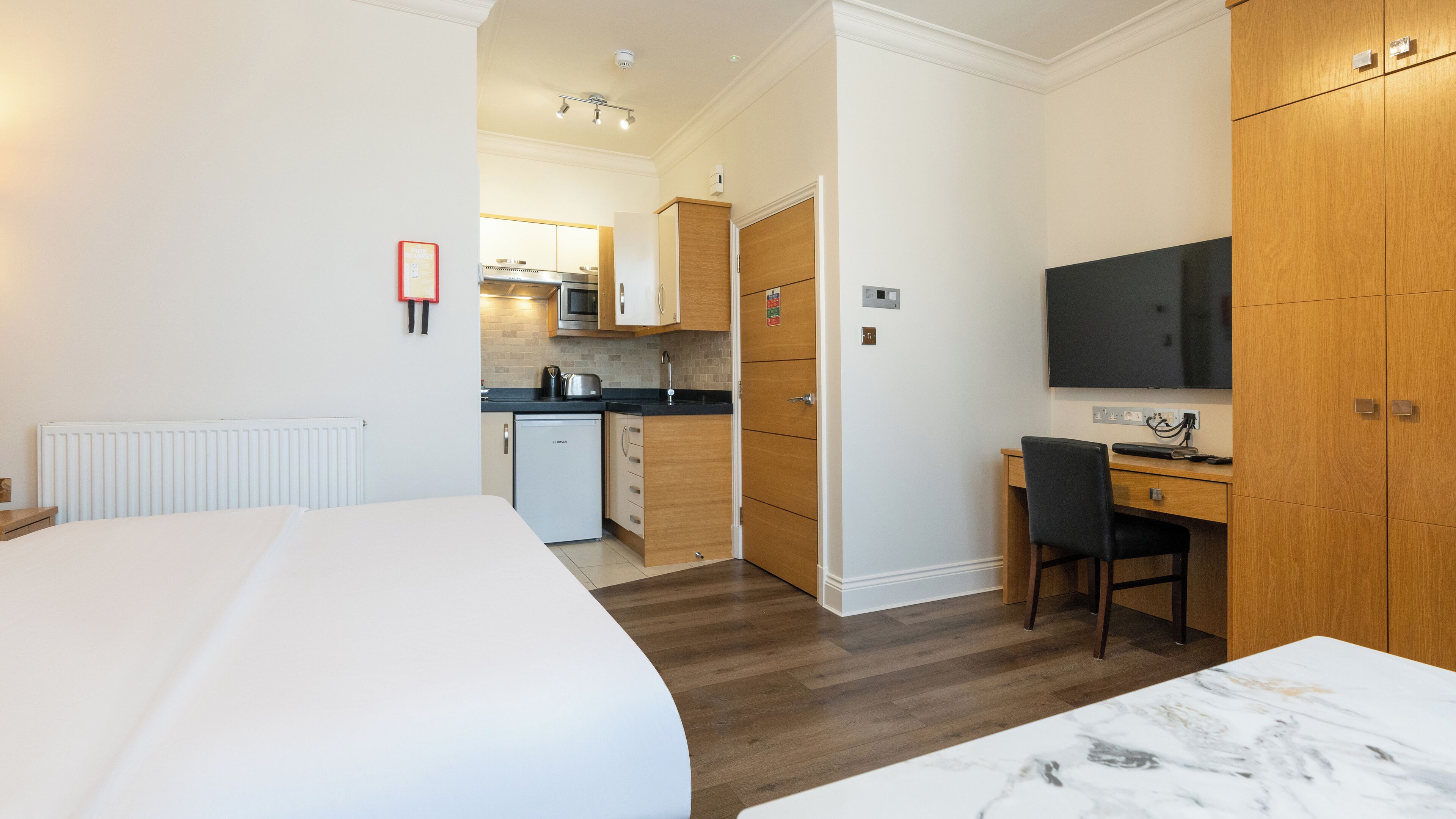 Une chambre d’hôtel comprenant un lit, un bureau avec une chaise, une télévision, un coin cuisine et une armoire.